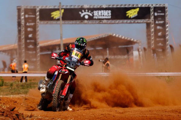  A equipe Honda Racing, detentora de um impressionante histórico de 11 títulos nas motos, abriu a disputa da 34ª edição do Rally dos Sertões 2026 com um desempenho avassalador. O espanhol Tosha Schareina, atual campeão e piloto da Monster Energy Honda HRC, destacou-se ao cravar os melhores tempos no prólogo e no subsequente Super Prime, realizado em Goiânia (GO). Sua performance não apenas o consagra como vencedor do Troféu Sylvio de Barros, mas também garante à equipe a pole position para a primeira etapa da competição, que parte de Goiânia em direção a Cavalcante (GO) neste domingo (23/8), consolidando a ambição de conquistar o 12º título sobre duas rodas.  Acelerando na liderança: O domínio da Honda no prólogo e super prime  As atividades de sábado (22/8) foram cruciais para definir a ordem de largada do maior rally das Américas. O prólogo, disputado nas primeiras horas da manhã, selecionou os oito pilotos mais rápidos que avançaram para o Super Prime. Este último, um embate eliminatório em formato mata-mata, cativou o grande público presente, que viu Tosha Schareina demonstrar sua maestria a bordo da Honda CRF450Rally. O piloto espanhol não apenas dominou as ações, mas também solidificou a posição da Honda na frente do grid, um passo fundamental para as ambiciosas oito etapas que se seguirão. Martim Ventura, o português que completa a formação internacional da Monster Energy Honda HRC, também garantiu sua vaga no grupo de elite ao conquistar a quarta posição no prólogo com sua Honda CRF450RXRally.  Destaques nacionais e a inovação da CRF300F  A representação brasileira da equipe Honda Racing também brilhou. O capixaba Bruno Crivilin, líder do Campeonato Brasileiro de Rally Raid, mostrou sua velocidade ao registrar o segundo melhor tempo no prólogo, pilotando a Honda CRF450RX Rally. Apesar de uma pequena queda no Super Prime ter o afastado das disputas finais, Crivilin celebrou a classificação entre os oito primeiros, garantindo uma posição de largada privilegiada para a primeira e desafiadora etapa. A inovação tecnológica e o talento nacional foram evidenciados com Alexandre Valadares “Brankim”, atual campeão nacional e do Sertões na classe Moto Brasil. Pilotando a Honda CRF300F, uma motocicleta off-road de fabricação nacional que faz sua estreia no Sertões, Brankim alcançou um resultado expressivo ao classificar a moto para o Super Prime, superando modelos de maior cilindrada e mostrando o potencial da engenharia brasileira. A goiana Bárbara Neves, em sua primeira participação na competição, confirmou o potencial da CRF300F ao registrar o segundo melhor tempo na categoria Moto Brasil, garantindo a 35ª colocação geral das motos.  O desafio do Sertões 2026: Rota, duração e logística  O Sertões 2026 não é apenas um palco para grandes disputas; ele é um dos maiores e mais desafiadores rallies das Américas, com mais de quatro mil quilômetros de percurso, sendo 2.611 quilômetros de trechos cronometrados distribuídos em oito etapas. A caravana atravessará paisagens diversas dos estados de Goiás, Bahia e Tocantins, exigindo máxima resistência e estratégia dos pilotos e equipes, até o encerramento do evento em 30 de agosto, novamente na capital goiana. A competição, que soma pontos decisivos para o Campeonato Brasileiro de Rally Raid, é um teste definitivo de máquina e piloto. A estrutura da Honda Racing Brasil de Rally, comandada por Dário Júlio Lopes desde 2013, conta com o suporte de importantes patrocínios que garantem a excelência e competitividade da equipe em todos os aspectos.  Vozes da equipe: Expectativas e primeiras impressões  Tosha Schareina expressou sua satisfação: “Estou muito feliz. No ano passado não comecei bem, mas agora ganhamos o prólogo e o Super Prime e é incrível estar aqui, com toda essa gente animando as disputas. Eu sempre tento levar no capacete ou na roupa algum detalhe do país em que estou competindo e desta vez quis homenagear o Brasil por meio da sua bandeira, porque guardo grandes lembranças do ano passado. A Honda Brasil me acolheu de forma incrível e tornou possível nossa participação nesta prova. É muito especial poder agradecer aos brasileiros dessa maneira”. Martim Ventura destacou a interação com o público: “Foi um dia muito bom de corrida, especialmente com o Super Prime, que trouxe grande envolvimento do público. É bem diferente das provas do Mundial, onde não temos tanto contato com as pessoas. Tudo correu bem, foi um momento mais de adaptação. O primeiro dia será longo e importante, então vou entrar com calma”. Bruno Crivilin mostrou pragmatismo: “O principal era estar aqui no Super Prime. Conseguir largar entre os oito primeiros é muito bom neste início. Já gastei a minha queda no Super Prime, agora vamos caprichar porque temos o dia mais longo pela frente e é quando a prova realmente começa”. Alexandre Valadares “Brankim” celebrou a performance da sua moto: “Muito satisfeito em colocar a CRF300F no Super Prime. Outras motos têm potência maior, mas a minha tem muita qualidade e está muito bem preparada. Agora vamos focar nos oito dias de prova e buscar o título”. Por fim, a estreante Bárbara Neves compartilhou sua emoção: “Foi difícil segurar a emoção, larguei no prólogo chorando, é a realização de um grande sonho estar aqui, ainda mais em Goiânia, que é a minha cidade. Eu me senti confortável com a planilha e com a moto, estou muito feliz. Espero fazer um bom rally”. As declarações refletem o entusiasmo e a concentração da equipe para o que promete ser uma edição histórica do Sertões.  Com um início poderoso e a liderança assegurada pelo campeão Tosha Schareina, a Honda Racing demonstra sua força e determinação em conquistar seu 12º título no Sertões. A combinação de talento internacional e a performance sólida dos pilotos nacionais, incluindo a surpreendente estreia da CRF300F, estabelece um cenário promissor para os próximos dias de competição. A jornada é longa e desafiadora, mas a equipe Honda Racing está pronta para enfrentar os mais de 4.000 quilômetros de trilhas, buscando solidificar sua posição como a maior vencedora da história do rally.  Fonte: https://mundopress.com.br
